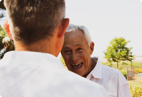 An older man smiling and speaking to a younger man. 